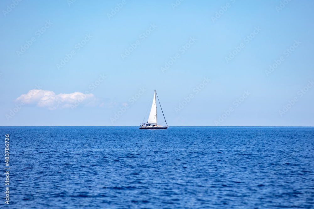 Sailing boat with open white sail, blue sky and rippled sea background