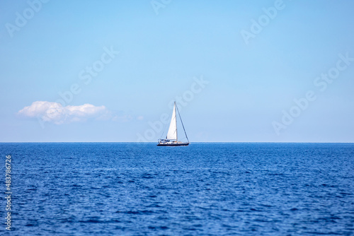 Sailing boat with open white sail, blue sky and rippled sea background