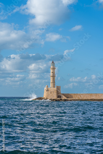 Lighthouse in the old venecian port in Chania, Crete during sunny summer day with blue splashing sea and blue sky