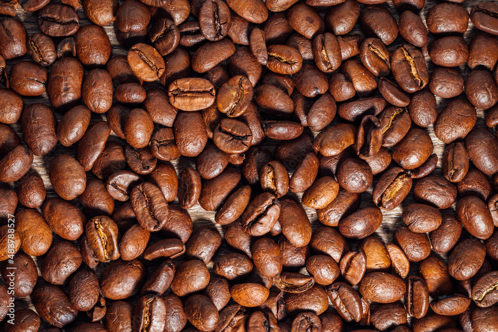 Naklejka premium Roasted coffee beans on dark brown wooden table. Top view on coffee beans on wooden background.