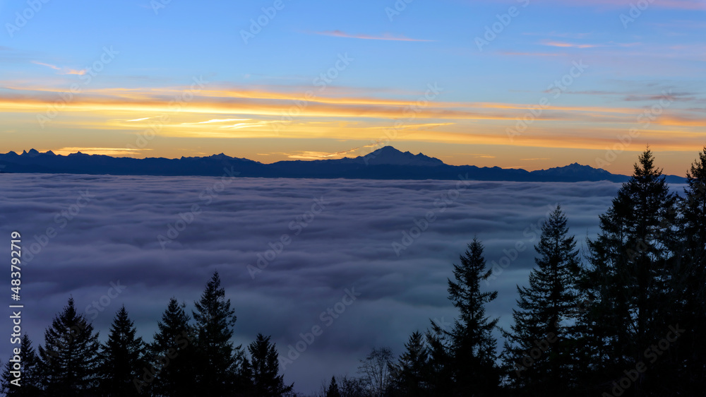Dense cloud cover over valley during winter inversion at sunrise, with mountains in silhouette on horizon.