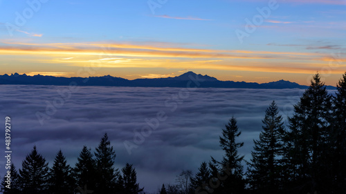 Dense cloud cover over valley during winter inversion at sunrise  with mountains in silhouette on horizon.