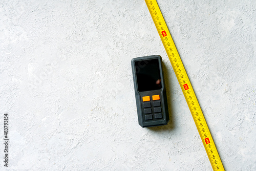 Classic mechanical tape measure and laser tape measure on a concrete background.