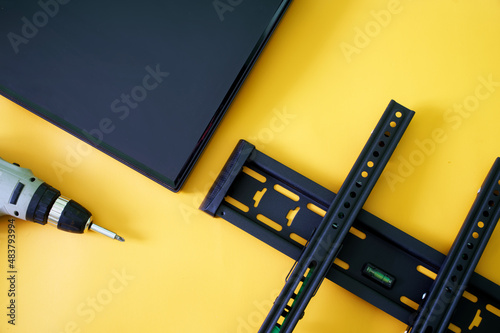 Bracket for wall mounting TV or monitor, screwdriver and monitor screen on yellow background. Concept of wall mounting computer monitor or TV in the interior office or home. Bubble level