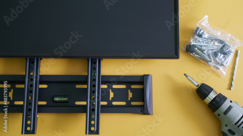 Bracket for wall mounting a computer monitor or TV, screwdriver, mounts and monitor screen on yellow background. Concept of wall mounting a computer monitor or TV in the interior
