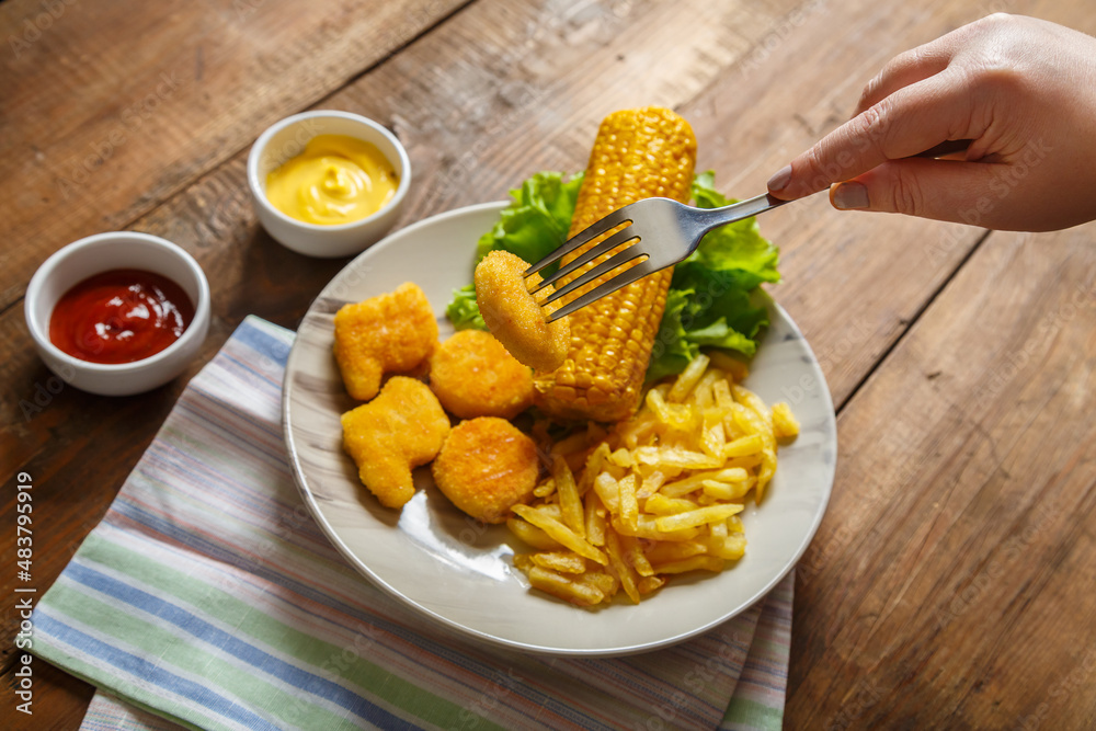 Nuggets, french fries and corn on the cob on lettuce leaves on a plate of nuggets on a fork.