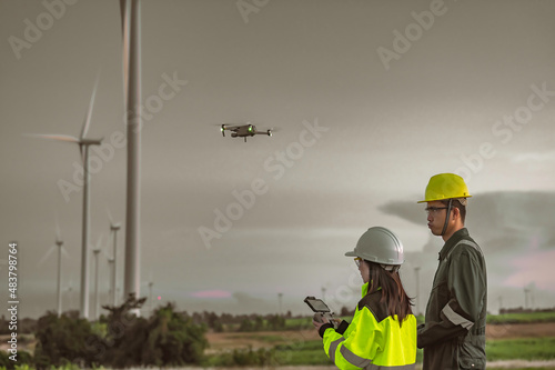 Two engineers working and holding the report at wind turbine farm Power Generator Station on mountain,Thailand people,Technician man and woman discuss about work.,Use drone view from high angle