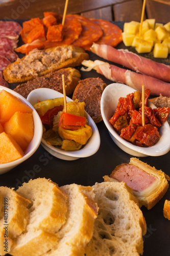 Italian antipasti wine snacks set. Brushettas, cheese variety, Mediterrnean olives, pickles, Prosciutto di Parma with melon, salami and wine in glasses over black grunge background. Top view