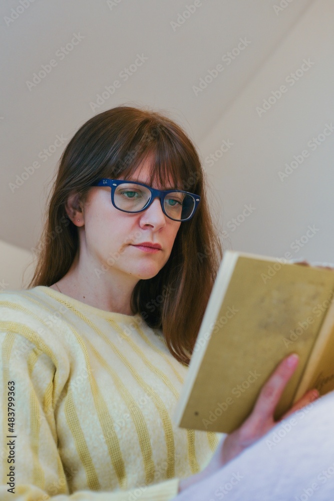 A woman sitting on the couch reading a book - obrazy, fototapety, plakaty 