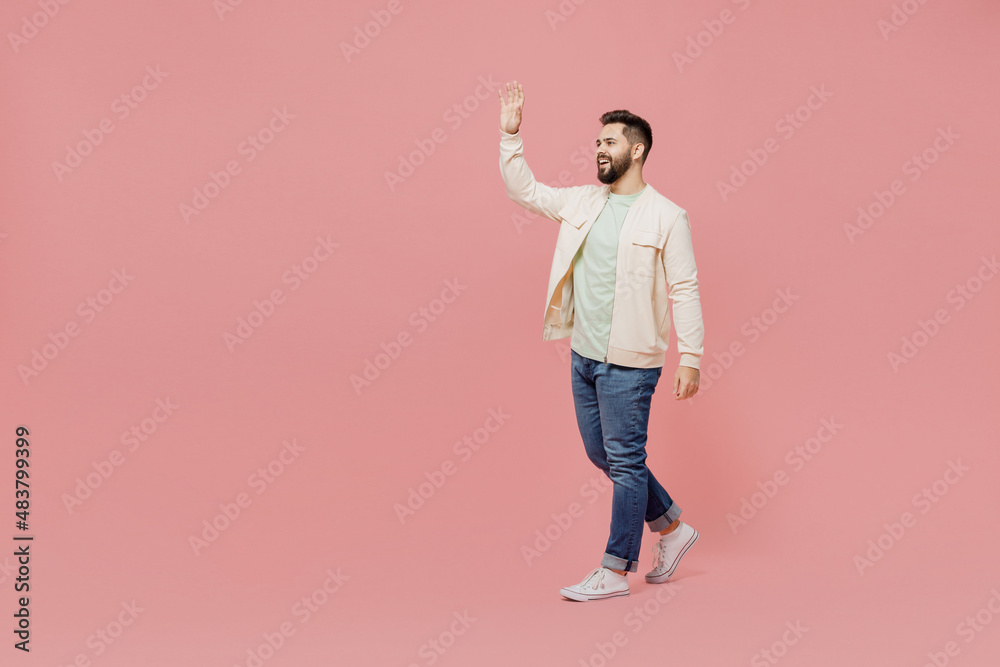 Full body young smiling cheerful friendly happy man 20s wear trendy jacket shirt walking go stroll waving hand isolated on plain pastel light pink background studio portrait. People lifestyle concept. Full body young smiling cheerful friendly happy man 20s wear trendy jacket shirt walking go stroll waving hand isolated on plain pastel light pink background studio portrait. People lifestyle concept.