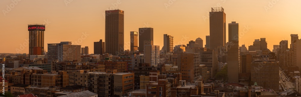 A horizontal panoramic cityscape taken during a golden sunset, of the central business district of the city of Johannesburg, South Africa