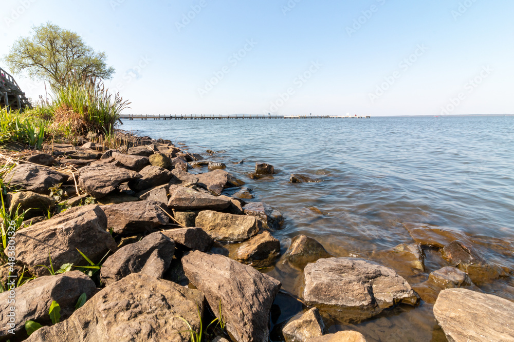 Shore with stones at the lake. A jetty in the background Shore with stones at the lake. A jetty in the background