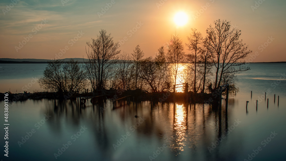 Obraz premium Headland with trees in the middle of the sea at sunset. reflection in the sea.