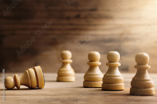 Wooden chessmen standing with one chess pawn lying.
