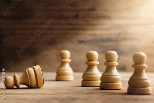 Fotografía Wooden chessmen standing with one chess pawn lying.