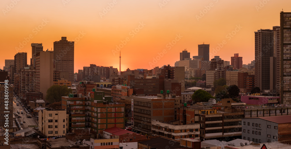 Obraz premium A horizontal panoramic cityscape taken at sunset, against an orange sky, of the central business district of the city of Johannesburg, South Africa
