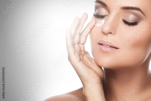 Beautiful woman applying moisturizing cream under her eye