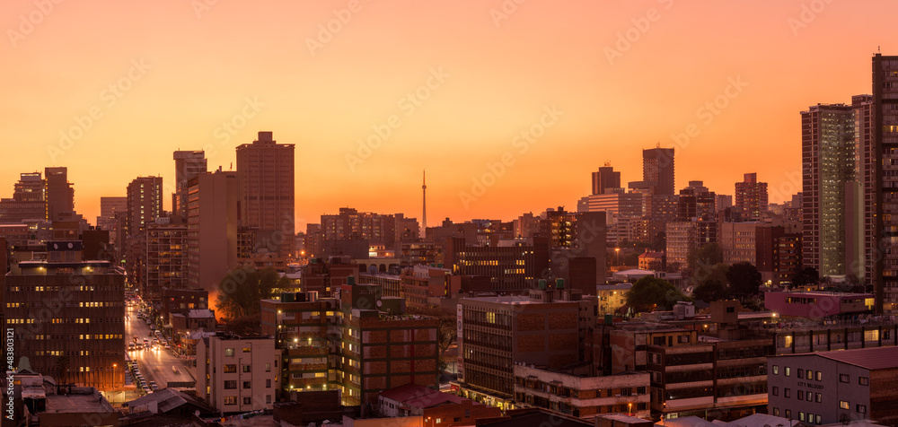 Fototapeta premium A horizontal panoramic cityscape taken after sunset, against a pink and orange sky, of the central business district of the city of Johannesburg, South Africa
