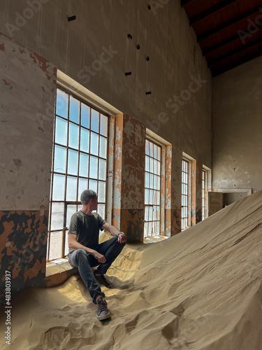 Young man in abandoned building posing in room. Ghost town Kolmanskop.