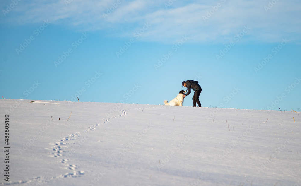 man and his happy white dog enjoying winter snow outdoors on sunny day