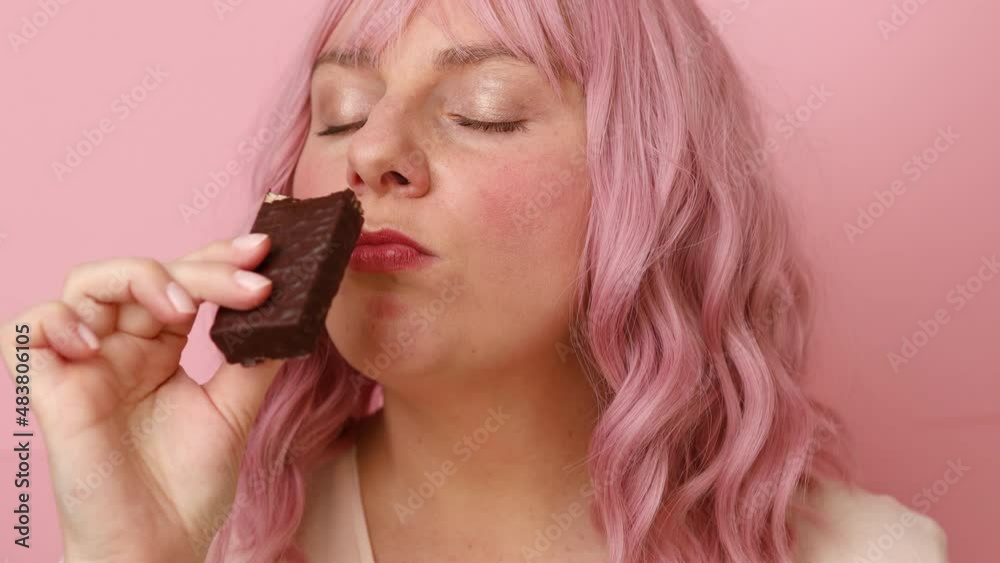 Young woman biting in a pieace of chocolate waffle candy isolated over pink background Young woman biting in a pieace of chocolate waffle candy isolated over pink background