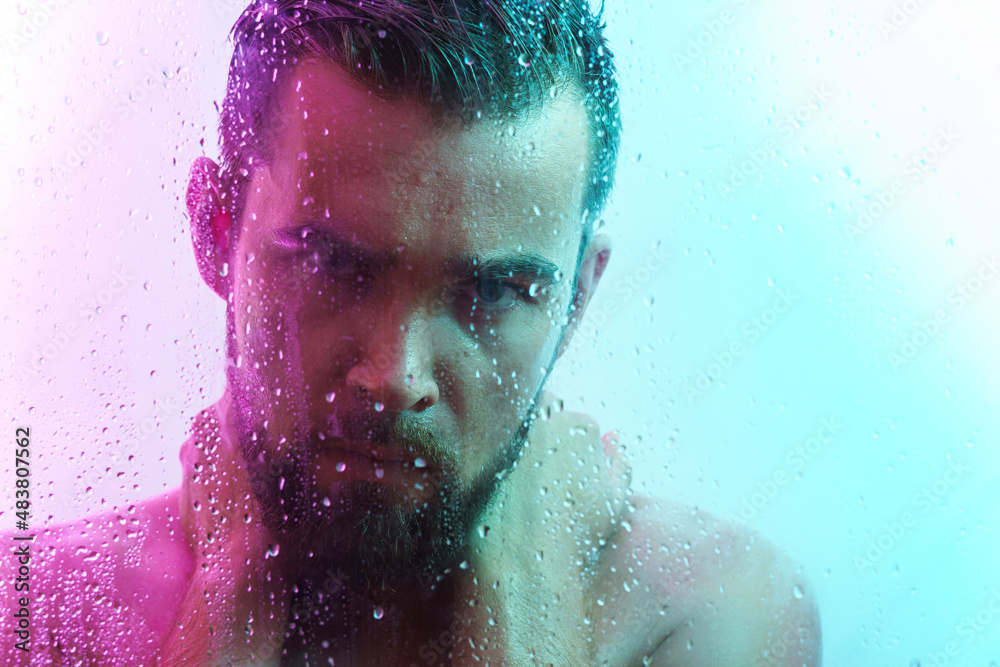 Portrait of handsome young man captured through wet glass in colorful light