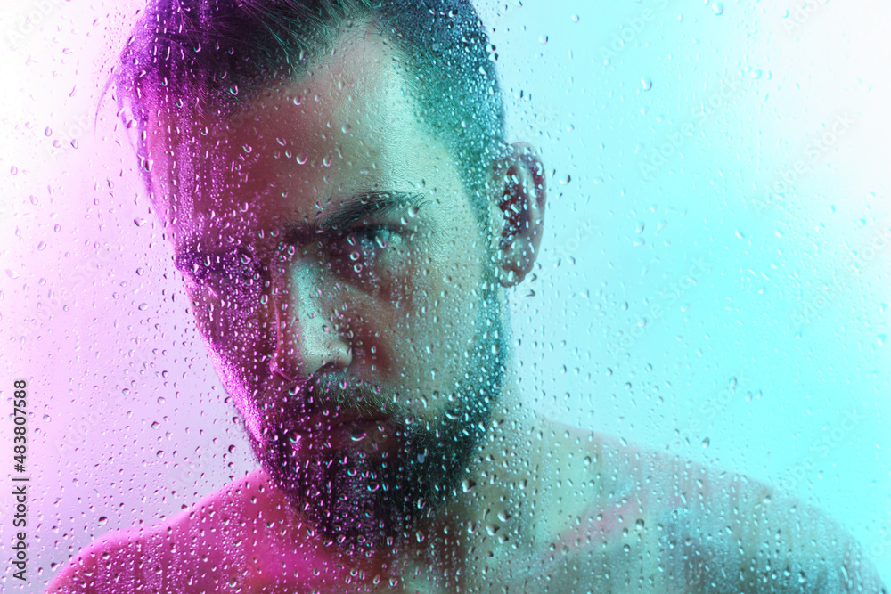 Portrait of handsome young man captured through wet glass in colorful light