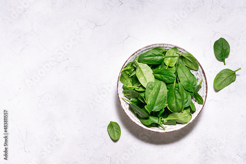Fresh raw baby spinach leaves in ceramic bowl on white marble background top view. Healthy diet food concept, copy space for your design.