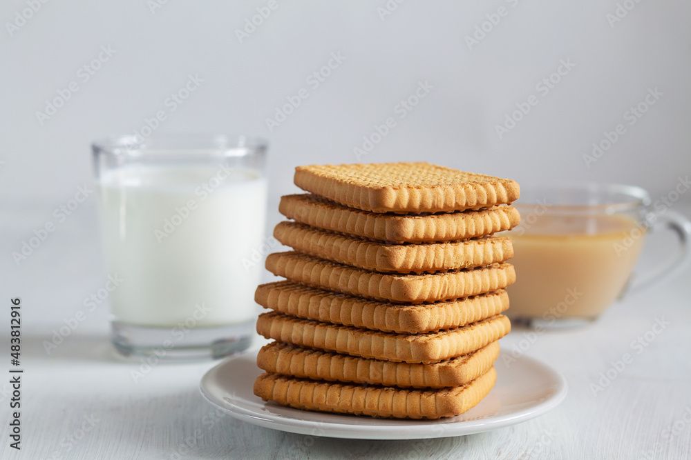 glass of milk and cookies.stacks of tasty cookies with tea on the white plate. square biscuits on the white table with copy space. healthy eating. glass of milk and cookies.stacks of tasty cookies with tea on the white plate. square biscuits on the white table with copy space. healthy eating.