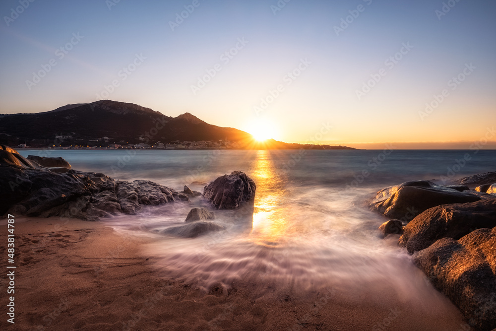 Sunset over a small sandy beach at Aregno plage in the Balagne region of Corsica with the village of Algajola in the distance