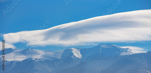 snow-capped mountain peaks with coniferous forests and clouds in the blue sky