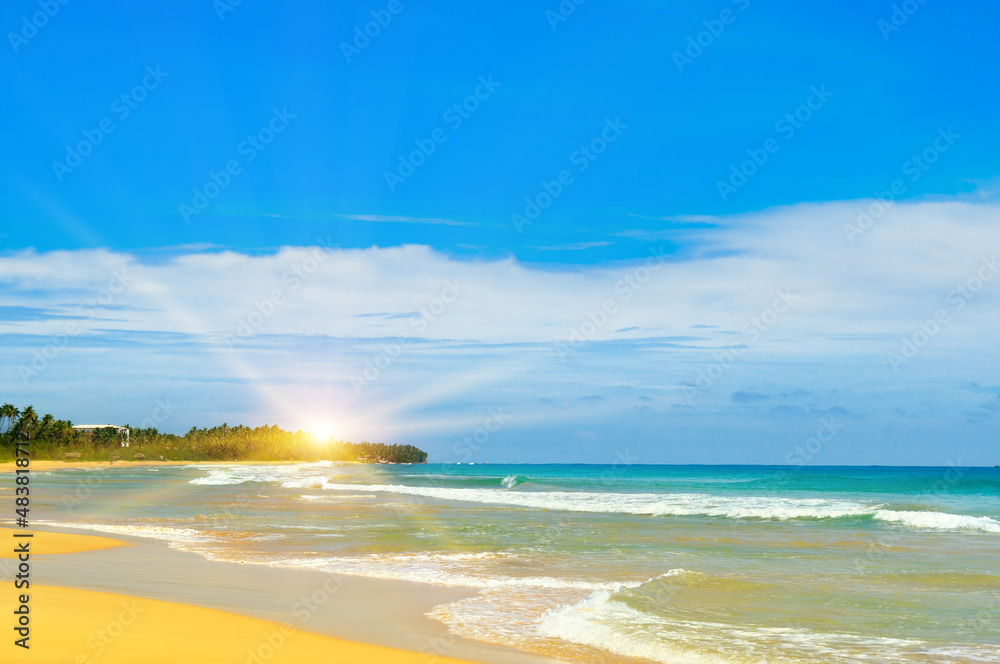 Sandy tropical beach, blue ocean water and bright sun rise.