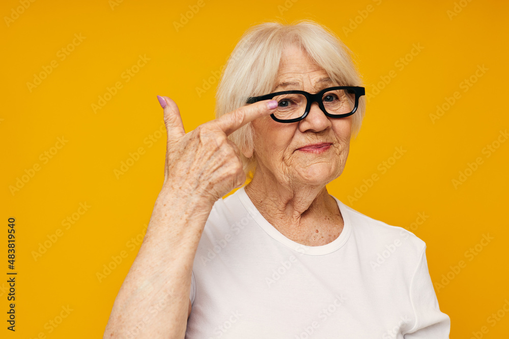 Photo of retired old lady in casual t-shirt and glasses yellow background Photo of retired old lady in casual t-shirt and glasses yellow background