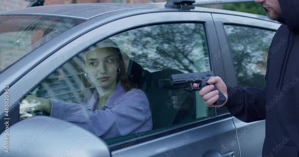 Dangerous criminal man with gun stealing car of scared young woman from outside, threats. Black male holding a pointed gun in glass of car to driver, hijacking, car theft, commit a crime Dangerous criminal man with gun stealing car of scared young woman from outside, threats. Black male holding a pointed gun in glass of car to driver, hijacking, car theft, commit a crime