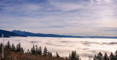 Dense winter cloud inversion seen from a mountaintop residence looks like stormy ocean with mountain backdrop in silhouette.