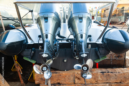 Two outboard motors at the stern of a motorboat resting on wooden blocks in dry dock. photo