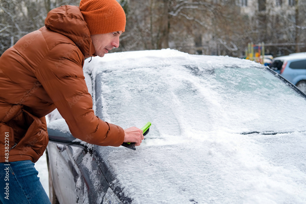 A man holds a brush in his hands and cleans the windows of the car from snow. The concept of transport, winter, weather, people and vehicles. A man holds a brush in his hands and cleans the windows of the car from snow. The concept of transport, winter, weather, people and vehicles.