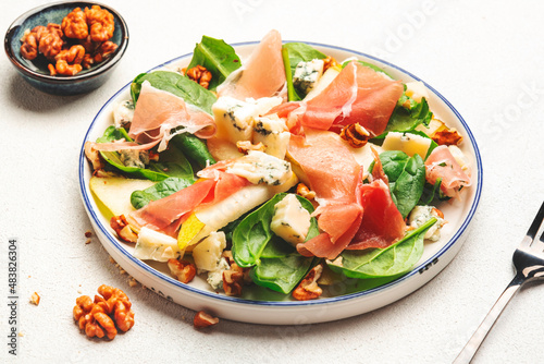 Summer pear salad with jamon, blue cheese, spinach and nuts on white table background, top view, copy space