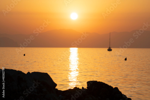 suggestivo tramonto di un sole meraviglioso verso la montagna evanescente con riflesso al centro dell'inquadratura sul mare verso uno scoglio scuro in primo piano , nave a vela , colore giallo photo
