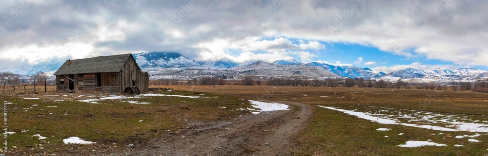 Panorama of field with house, trees and hills with snow in the winter