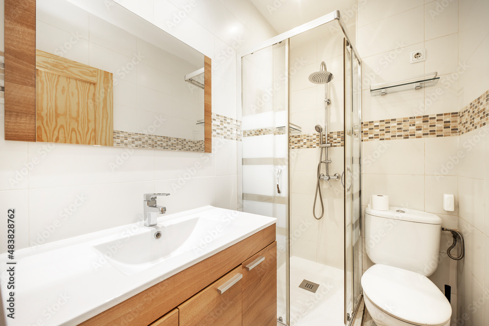 Conventional toilet with wooden furniture, elongated white sink and square shower cabin with screen Conventional toilet with wooden furniture, elongated white sink and square shower cabin with screen