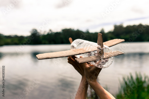 children's hands playing with a plane built with recycled material (wood, PVC bottles, cardboard)