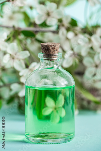 Aromatic essential oil in glass bottle and flowers on blue background. Aromatherapy and spa concept. Refreshing fragrances for relaxation.