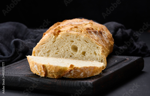 baked whole oval bread made from white wheat flour on a black table, fresh pastries