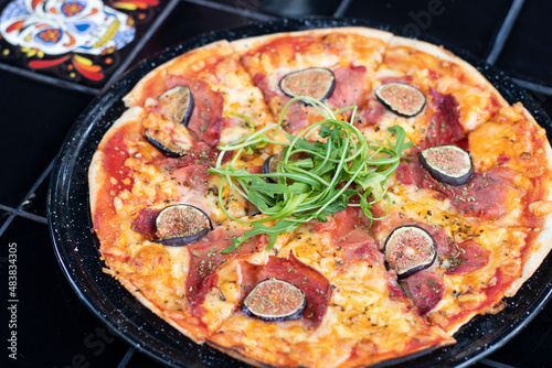 Pizza de jamón serrano con higos y arúgula sobre mesa negra  photo
