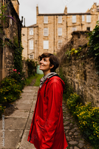 Young female posing with a red raincoat in the middle of a close during a rainy summer day in Edinburgh.