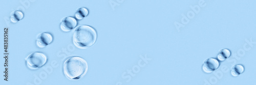 Banner made with cosmetic hydrating product or ingredient concept. Blue drops of transparent liquid on a light background. Drops gel or oil close up. Abstract backdrop.