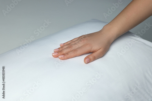 Woman touching soft white pillow on bed, closeup