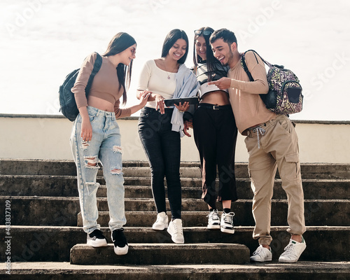 College friends smiling while looking at something on a tablet