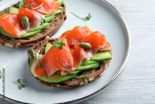 Delicious sandwiches with salmon, avocado and capers on white wooden table, closeup